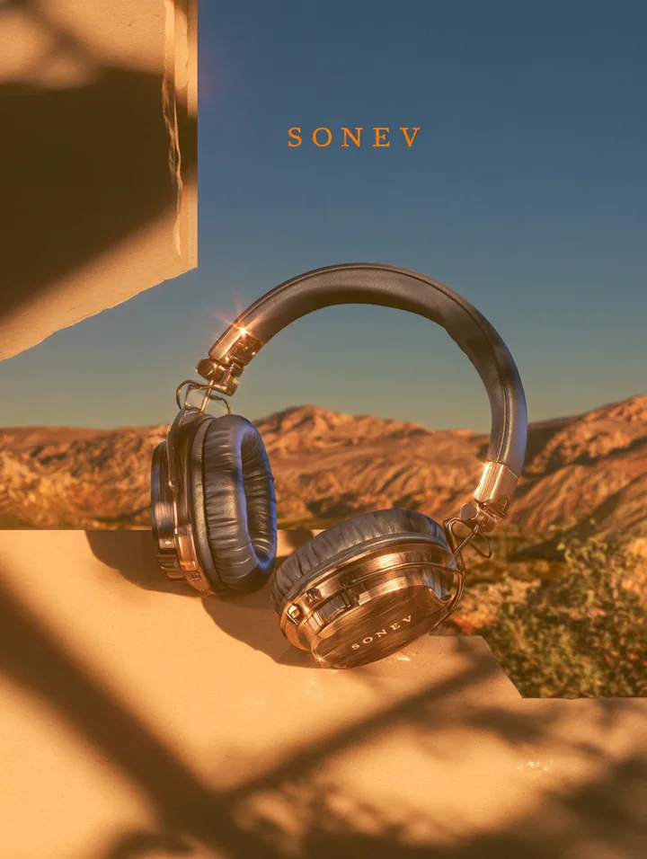 Premium over-ear headphones on warm architectural stone with mountains and blue sky behind