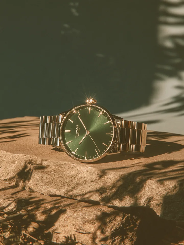 A gold metal wristwatch with a green dial resting on layered stone in sunlight